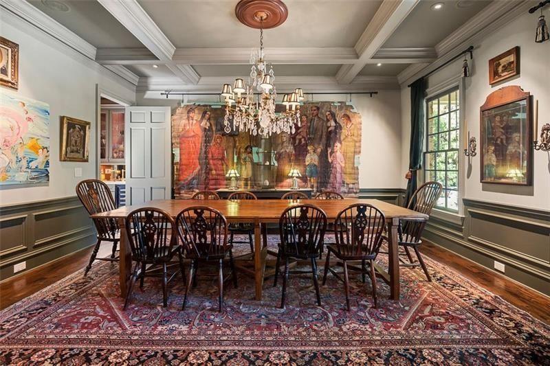 Coffered ceilings, deep wall molding, and darker trim details give the room a more defined look, while a crystal chandelier hangs directly above the long wood dining table at the center of the space.