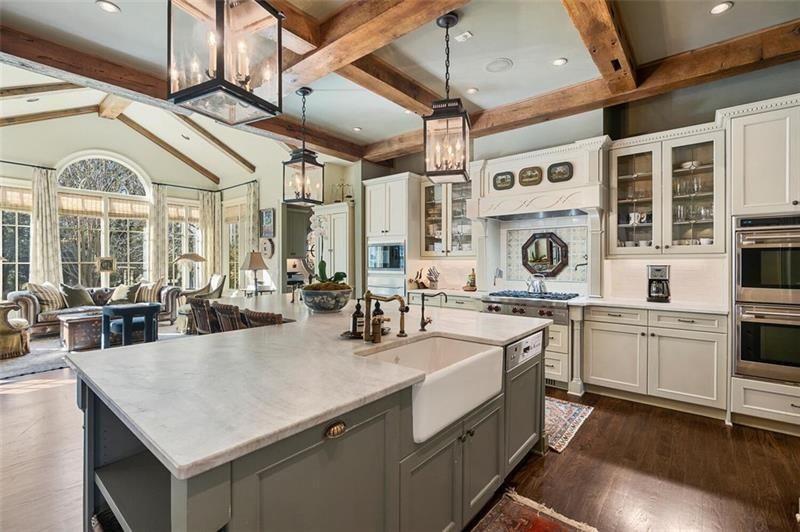Glass-front cabinets, integrated appliances, and open shelving keep the room functional without breaking up the clean design, while the farmhouse sink positioned at the island faces outward toward the nearby sunlit lounge.