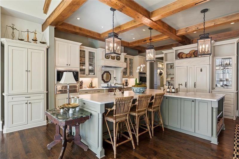Custom cabinetry wraps nearly every wall of the kitchen, combining cream-colored millwork with muted sage-toned island bases and marble countertops. 
