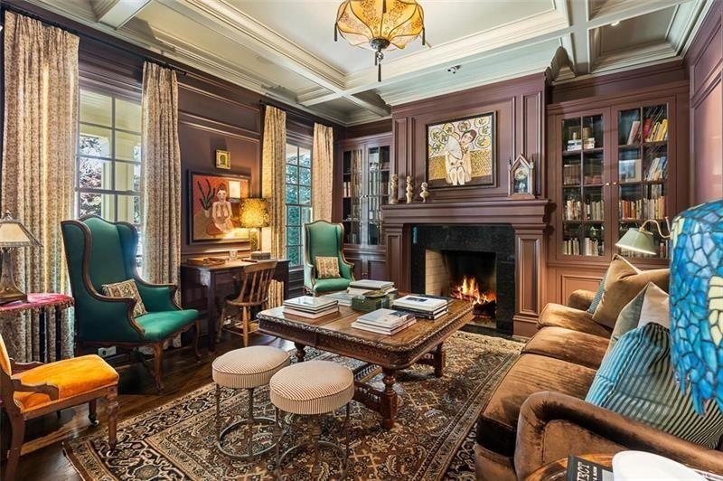 The seating arrangement centers around a carved wood coffee table layered with books and decor, surrounded by velvet wingback chairs, patterned rugs, and oversized sofas.