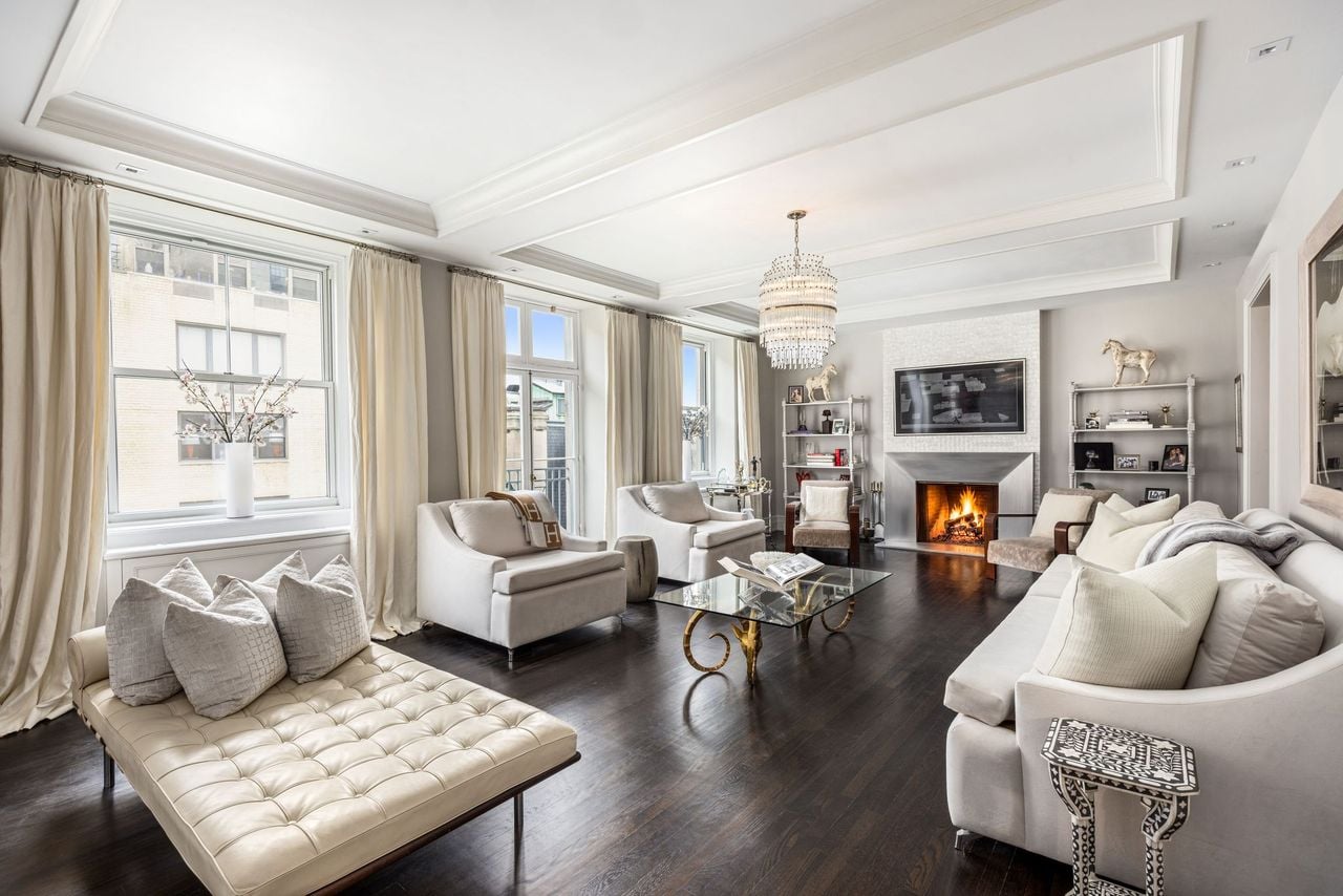 The living room opens into a bright and open entertaining space where oversized windows and French doors draw natural light across the dark-stained hardwood floors.