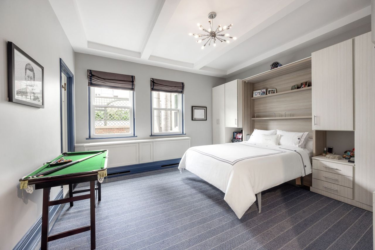 The primary suite's bedroom is finished in a softer palette of gray, white, and navy accents, with oversized windows bringing in natural light across the coffered ceiling and wide carpeted floors. 