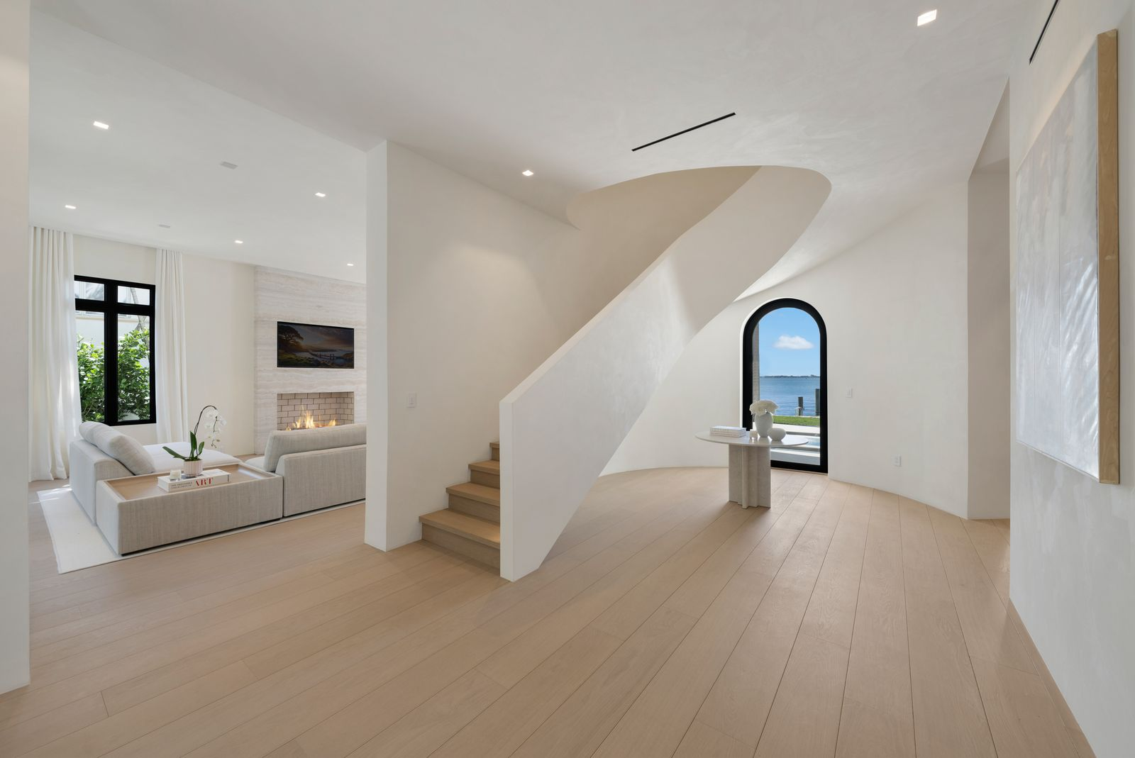 The central staircase curves upward as a sculptural focal point, while textured Marmorino plaster walls and pale wood flooring keep the focus on light and scale. 