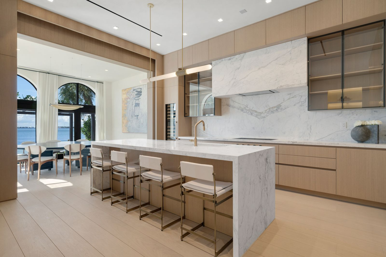 Down the hall, the kitchen shifts into a warmer palette with floor-to-ceiling ITALKRAFT cabinetry and oversized slabs of veined marble that wrap the backsplash, counters, and waterfall island. 