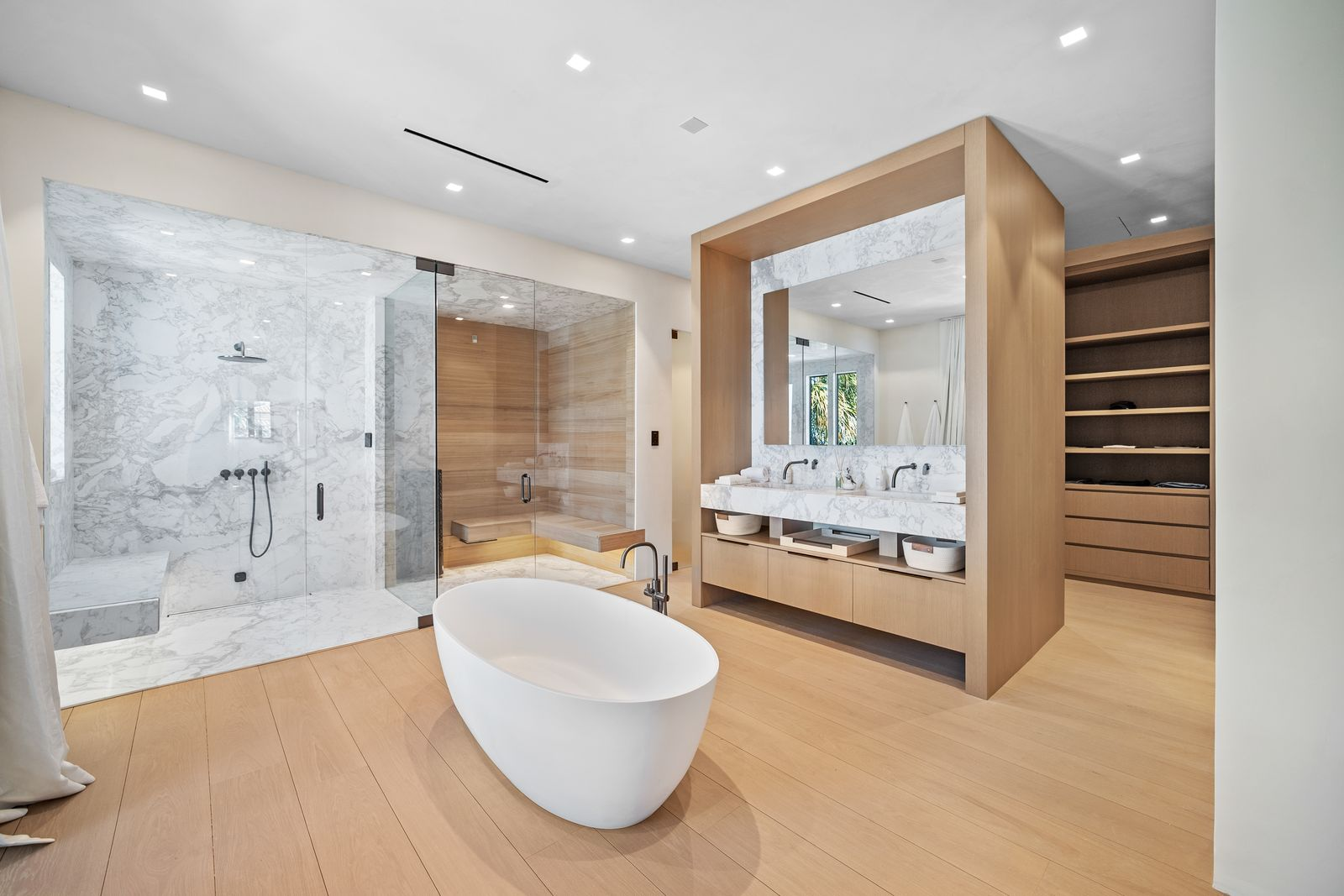 Inside the suite's bathroom, large slabs of marble wrap the walk-in shower and steam room, contrasting against warm wood detailing integrated into the sauna and custom vanity. 