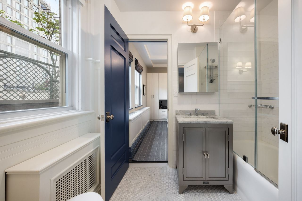 The marble bathroom continues the apartment’s polished renovation with heated floors, clean-lined cabinetry, and a soaking tub positioned beneath glass shower panels. 