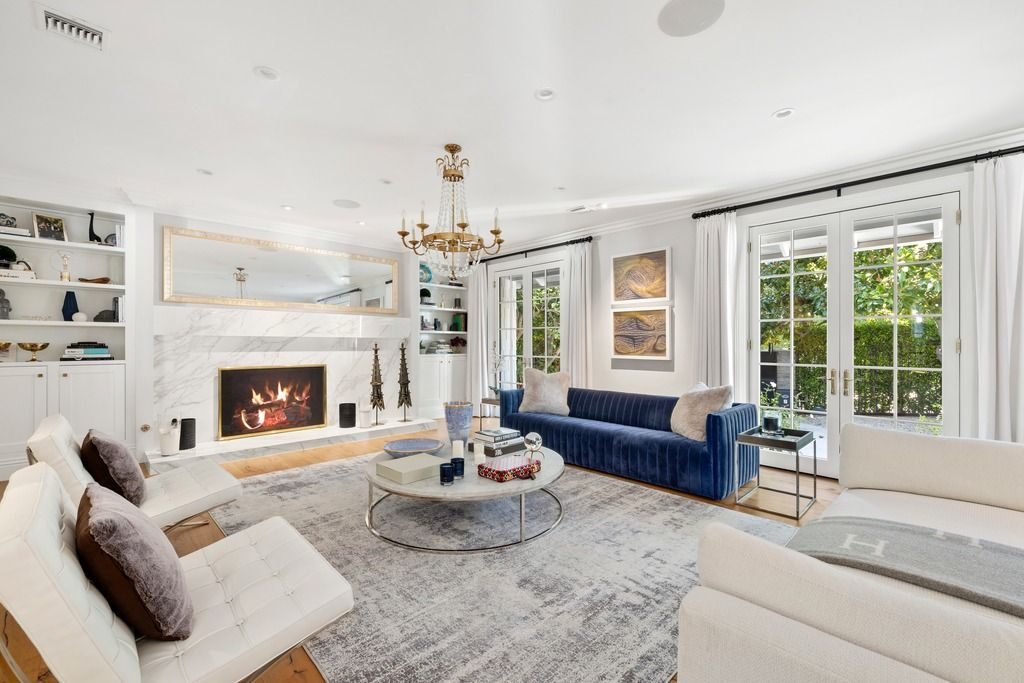 Seating is arranged around a circular coffee table, with a deep blue velvet sofa adding contrast against the lighter palette of white chairs, pale rugs, and linen drapery.