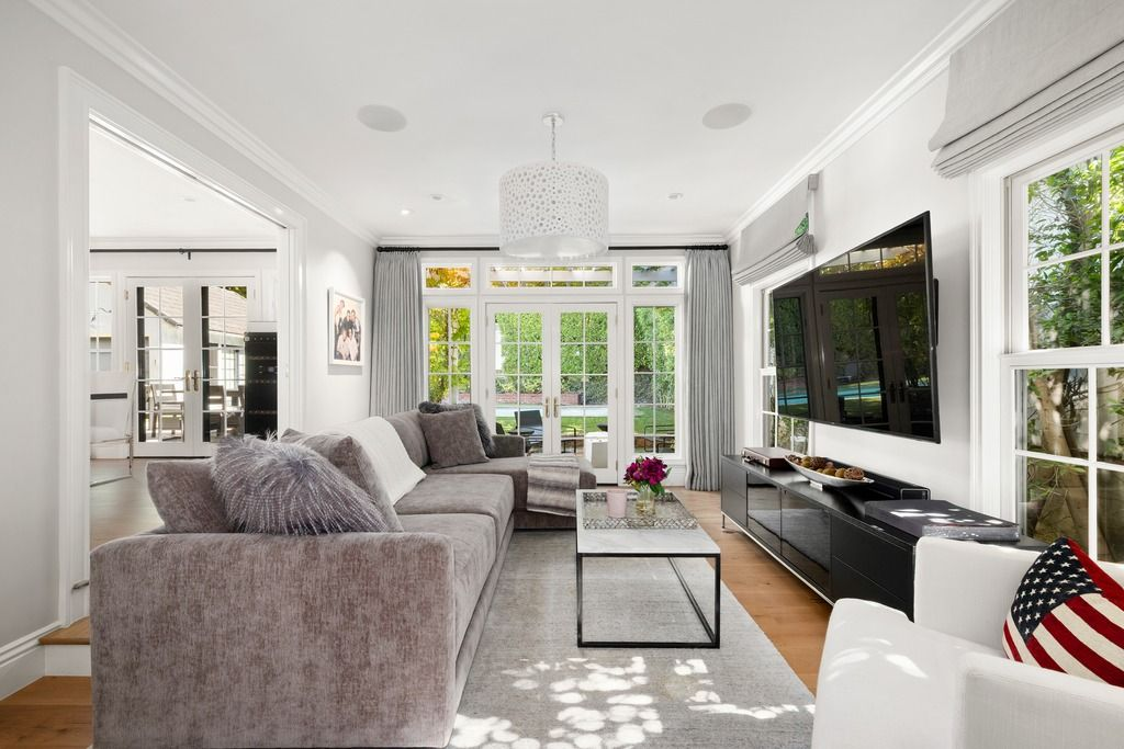 In the next room, the home transitions into a more casual media lounge centered around a large wall-mounted television and oversized sectional seating.