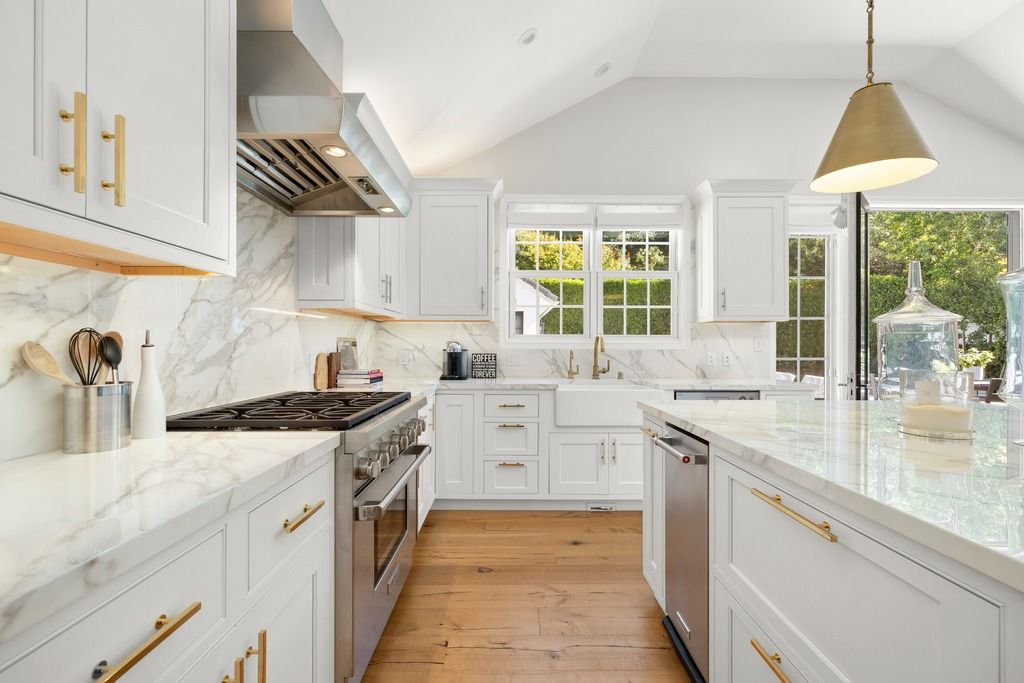 White cabinetry and marble-style surfaces give the room a clean, updated look, while brass hardware and pendant lighting add warmth throughout the space.