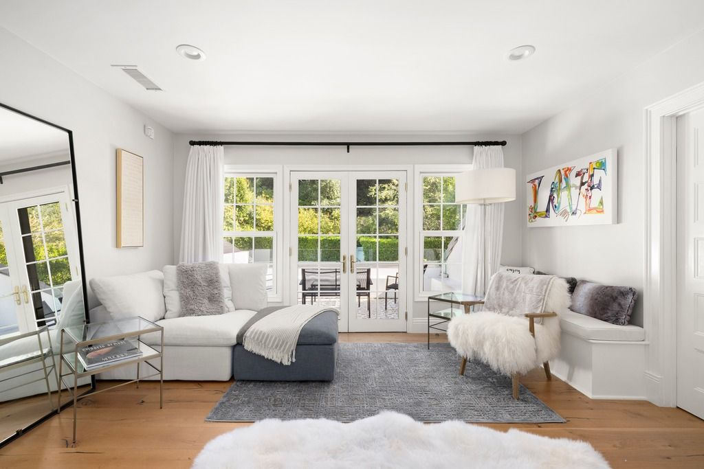 A lounge area on one side of the bed creates a secondary sitting space within the suite, furnished with a chaise, accent chairs, and layered textiles that soften the room’s clean lines.