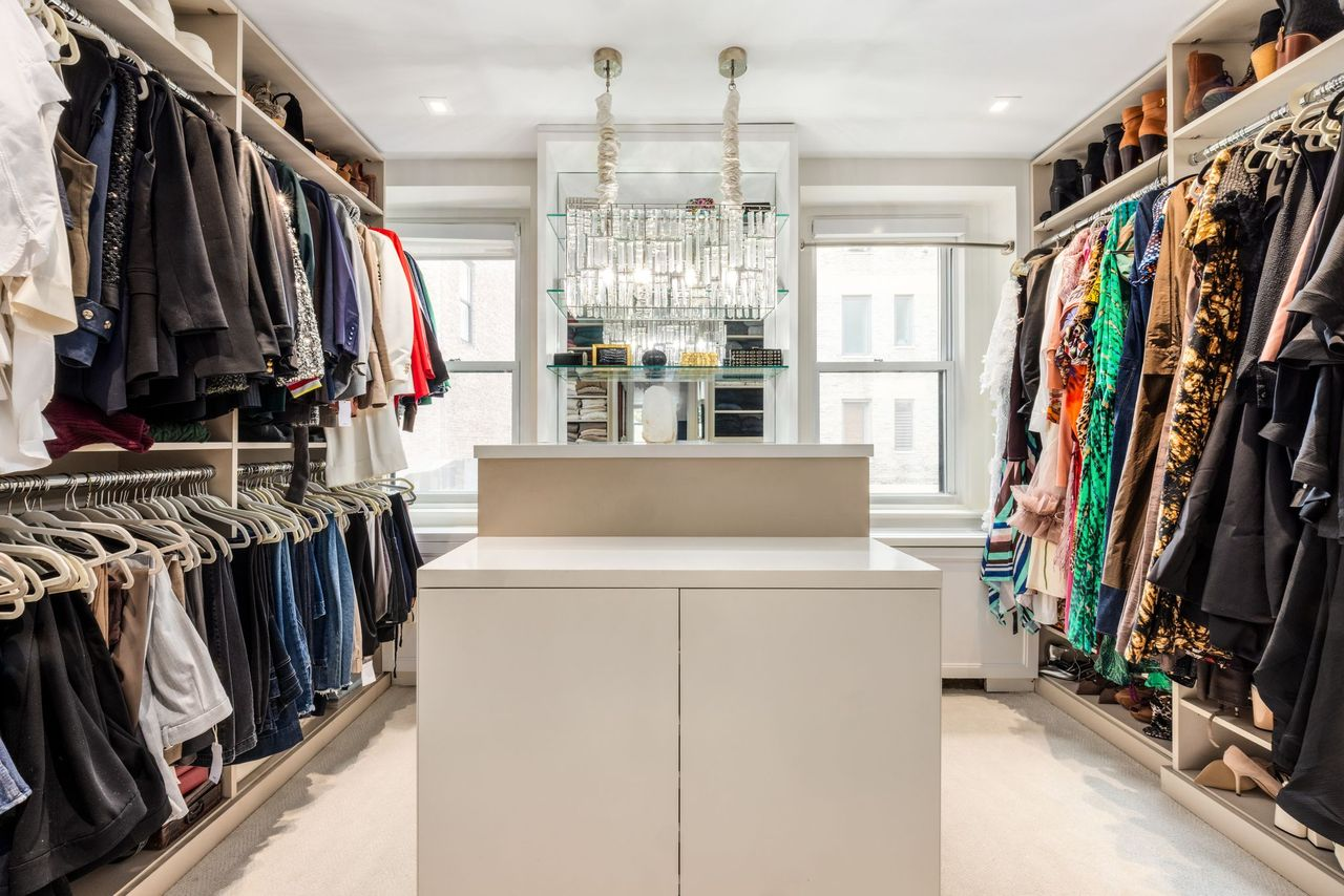 Double rows of custom storage line both sides, with hanging racks, shelving, and drawers organized around a central island beneath mirrored display shelving and pendant lighting.