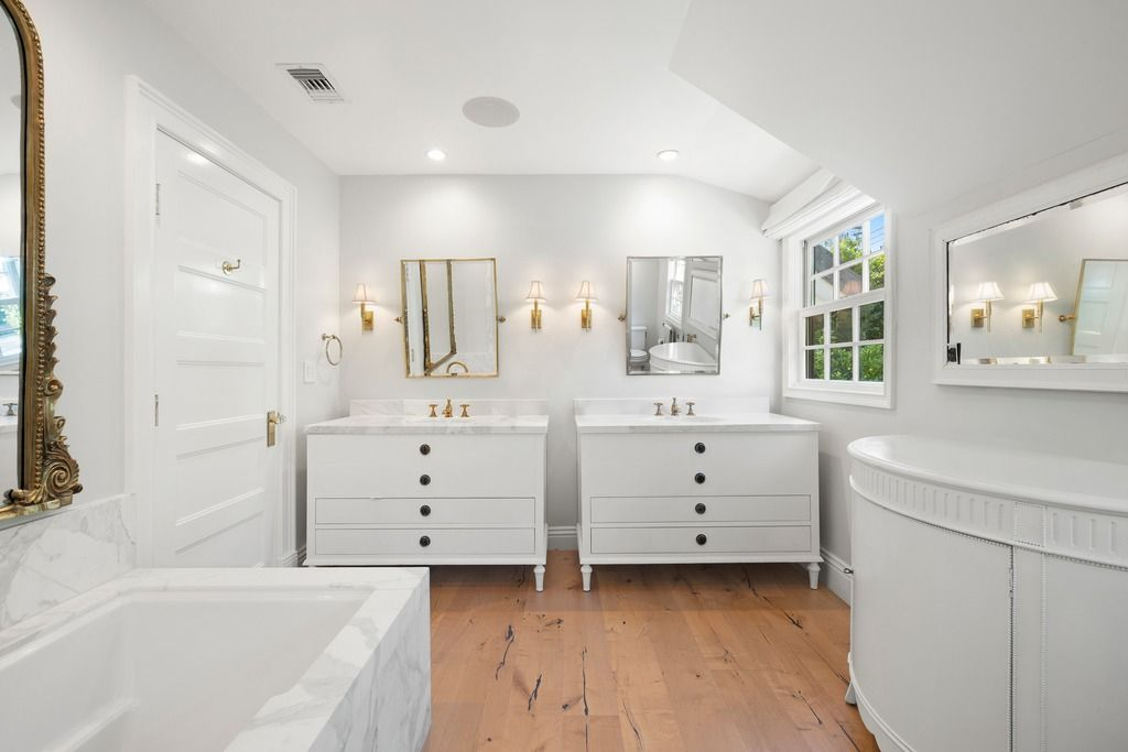 Dual vanities line the opposite wall under vaulted ceilings and skylight-style windows, bringing additional natural light into the space and reinforcing the bathroom’s open, airy feel.