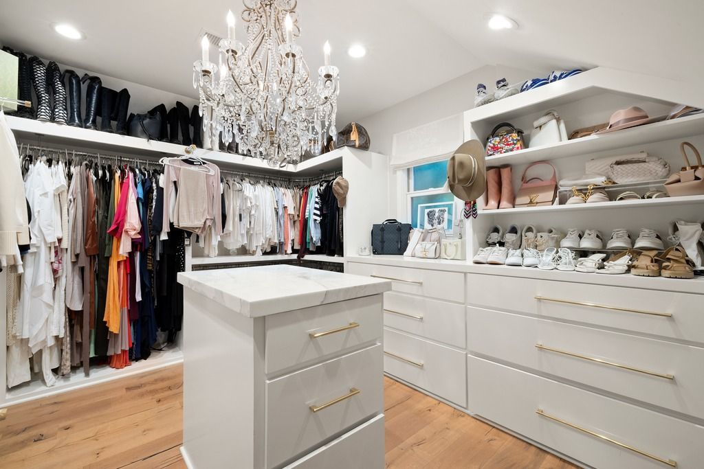 Connected to the suite is a large walk-in closet finished with custom white built-ins, brass hardware, and open shelving for shoes, handbags, and accessories.
