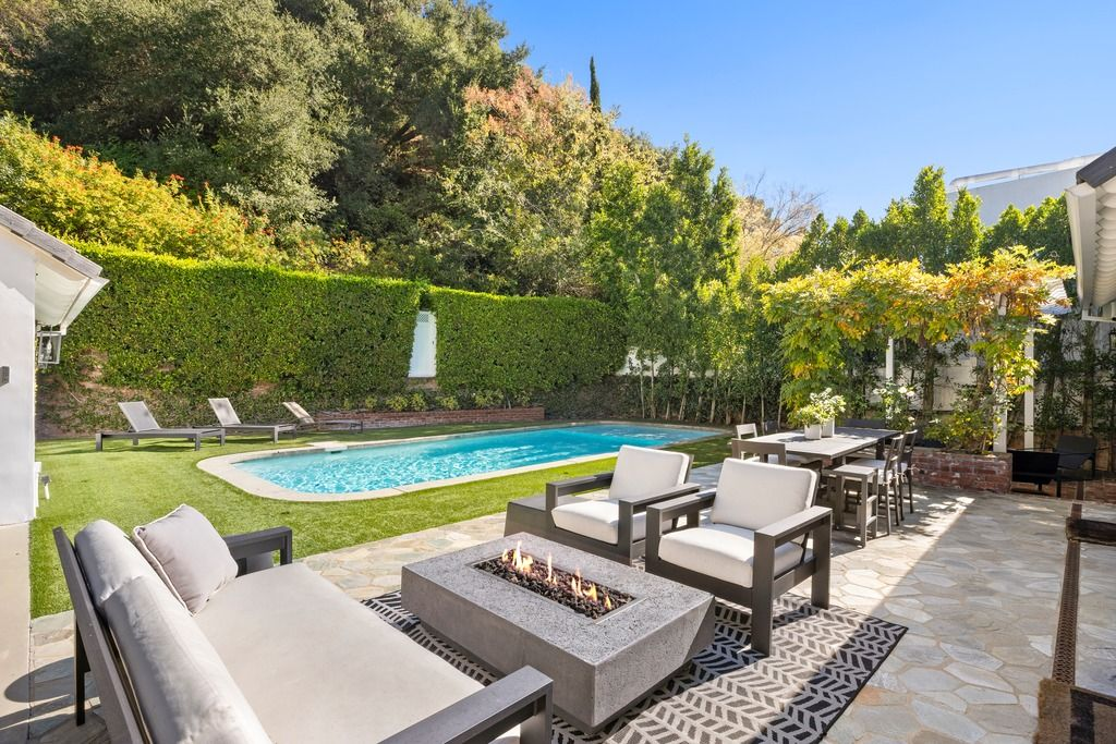 Just outside the house, the backyard begins with a stone patio arranged around a rectangular firepit lounge and outdoor dining area.