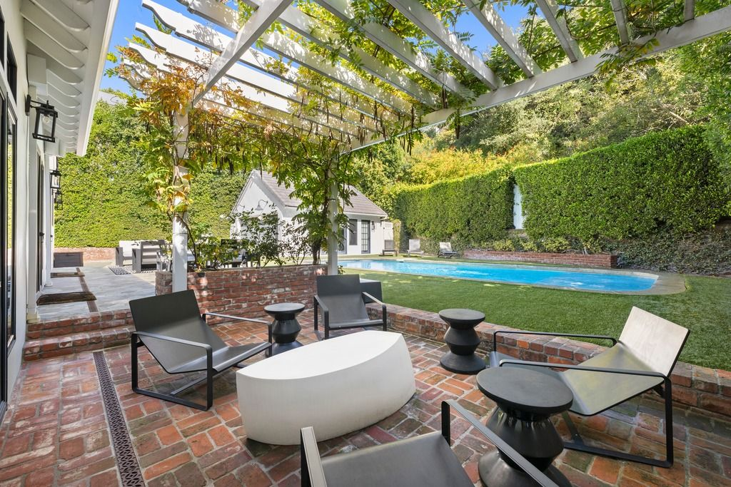 Along the side of the home, a pergola-covered terrace adds a more tucked-away sitting area finished with brick flooring and low modern lounge chairs.