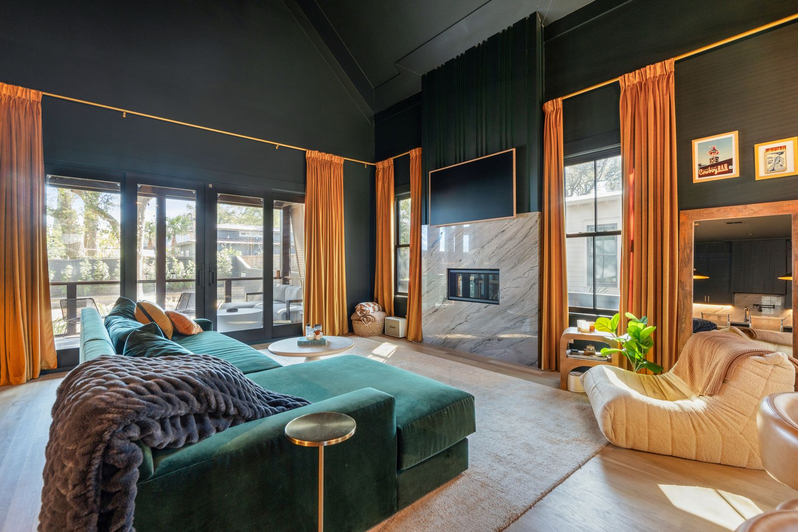 Across from it, a marble fireplace rises toward the ceiling with a mounted television above, creating a focal point that balances the room’s height with warmer natural textures.