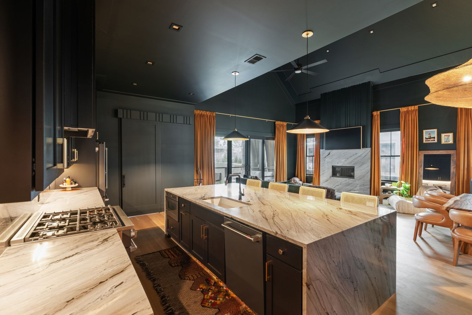 Pendant lights hang low over the island, adding a softer glow against the black ceilings and cabinetry, while integrated appliances blend directly into the cabinetry walls, helping the kitchen maintain its clean look.
