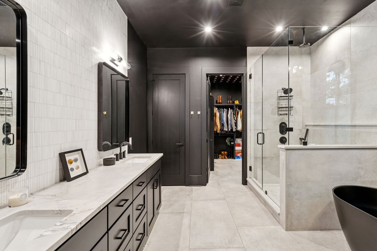 The bathroom shifts into a more minimalist modern look, combining oversized stone tile with matte black fixtures and streamlined cabinetry. 