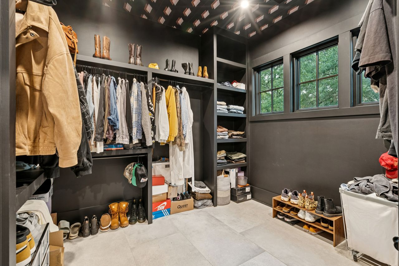 Open storage wraps around the room from floor to ceiling, organizing clothing, shoes, and accessories while maintaining the same aesthetic used throughout the suite.