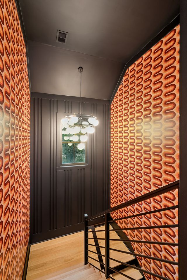 A staircase wrapped in retro-inspired patterned wall coverings with warm orange tones that contrast against the darker trim and lighting. 