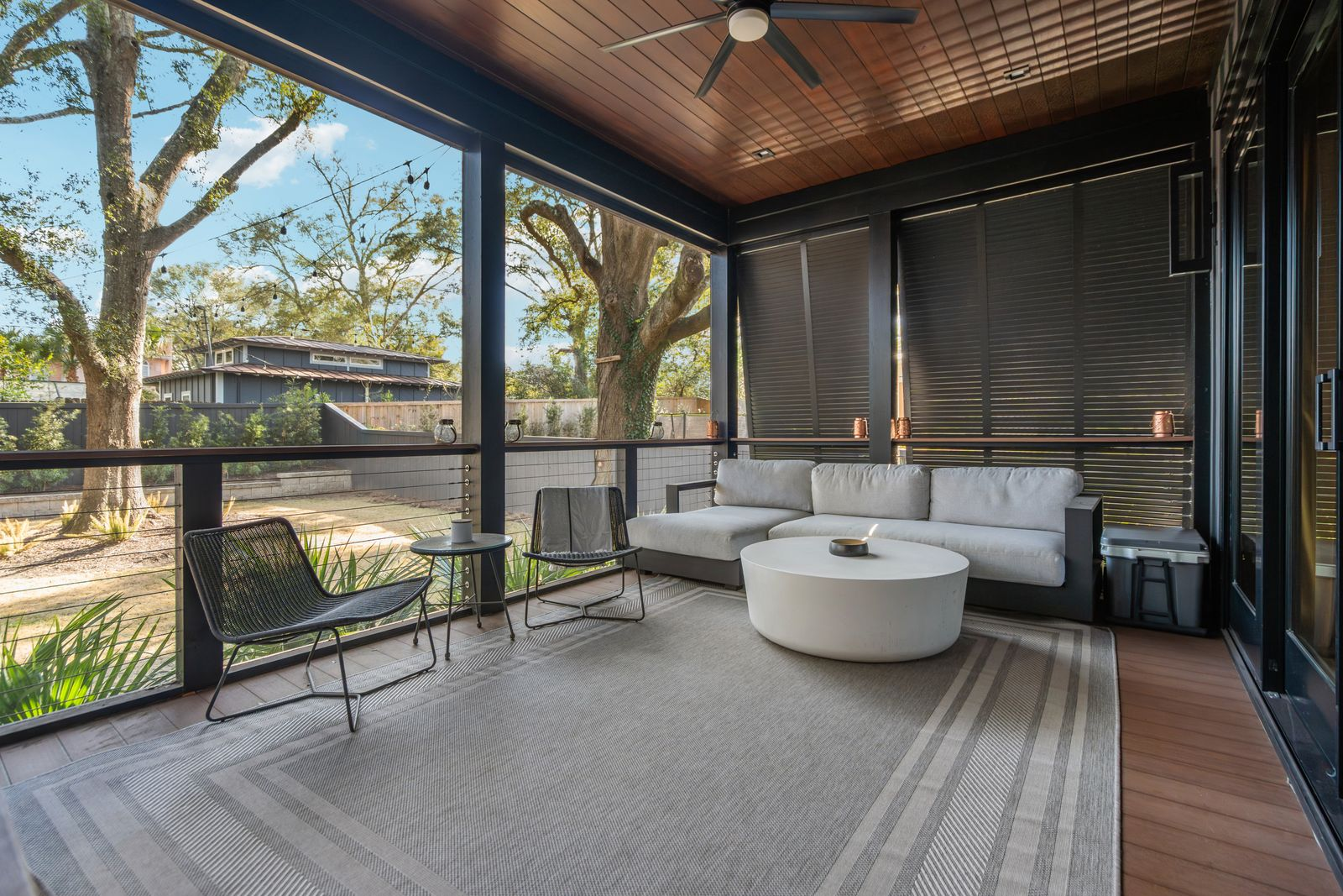 Just off the living room, a screened porch creates an extension of the main entertaining space with dark trim, a wood-paneled ceiling, and oversized openings that frame views of the yard. 