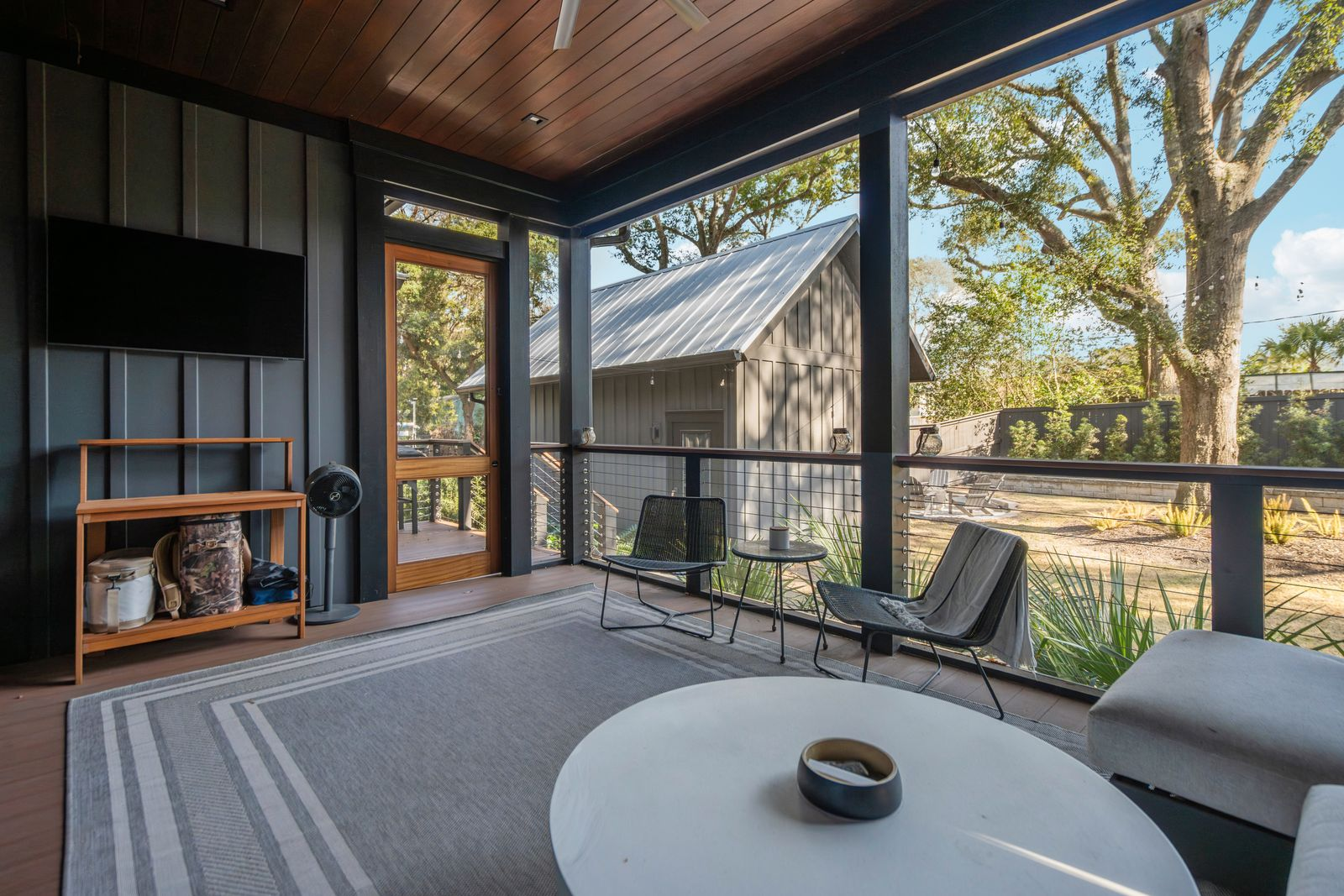 Lounge seating is arranged around a low circular table beneath ceiling fans and mounted televisions, making the space usable year-round.