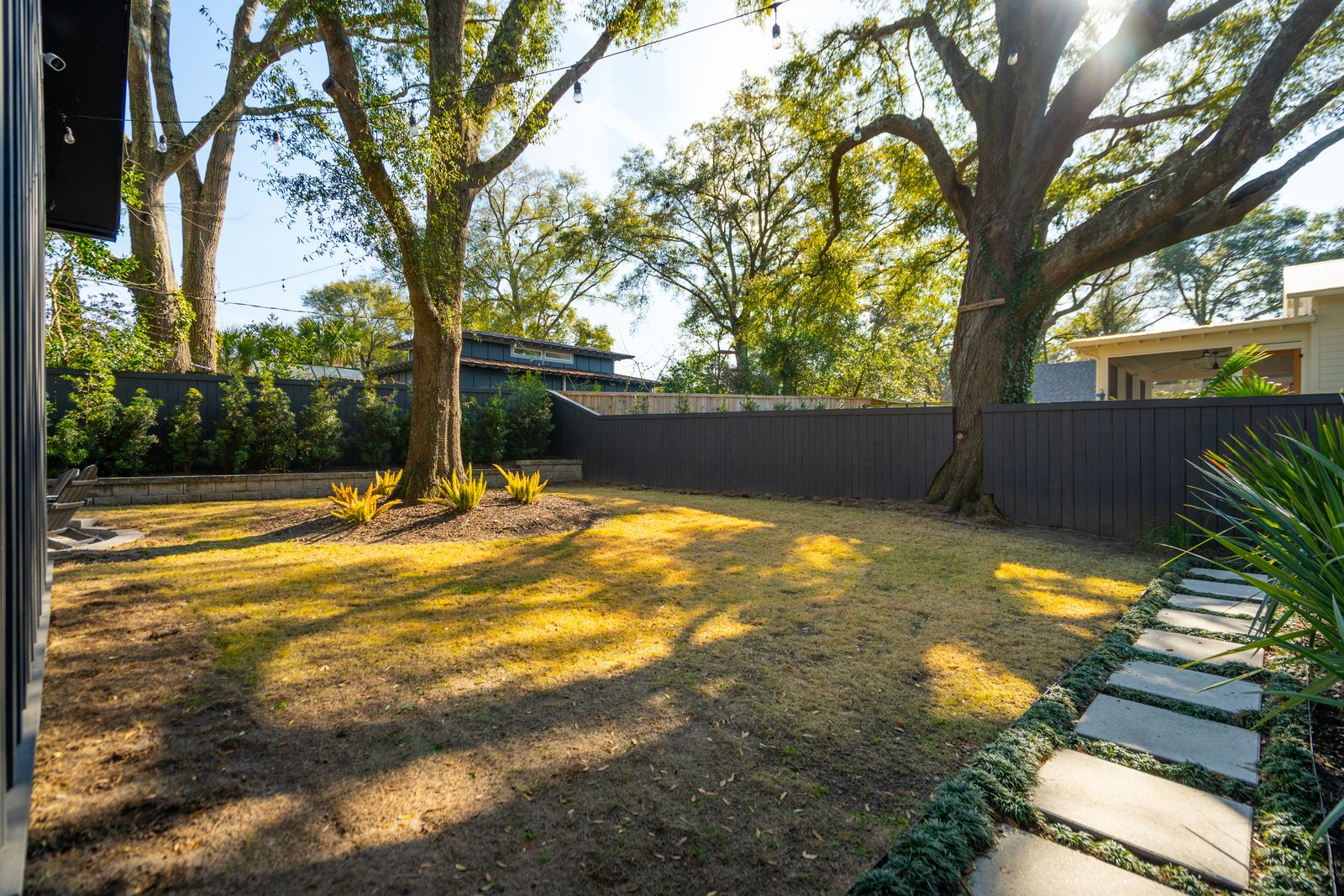 The open grassy area gives the property a quieter, more relaxed feel compared to the darker and moodier interiors, while black fencing and planted borders create separation around the perimeter.