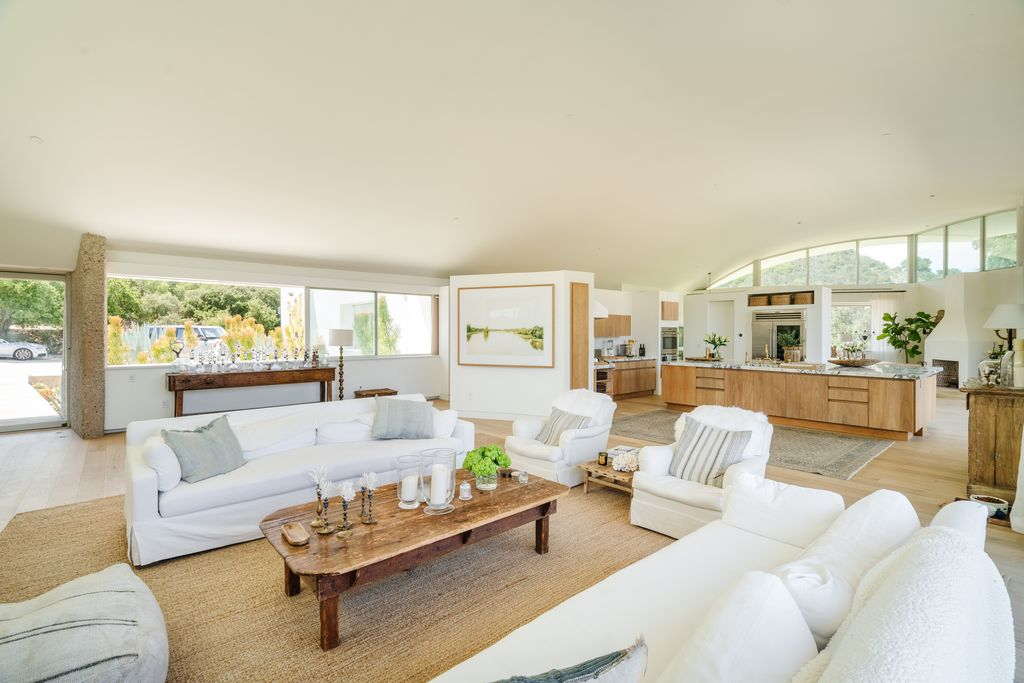 The interiors are warm, with pale wood flooring, linen-covered seating, and rustic wood accents softening the home’s modern architecture.