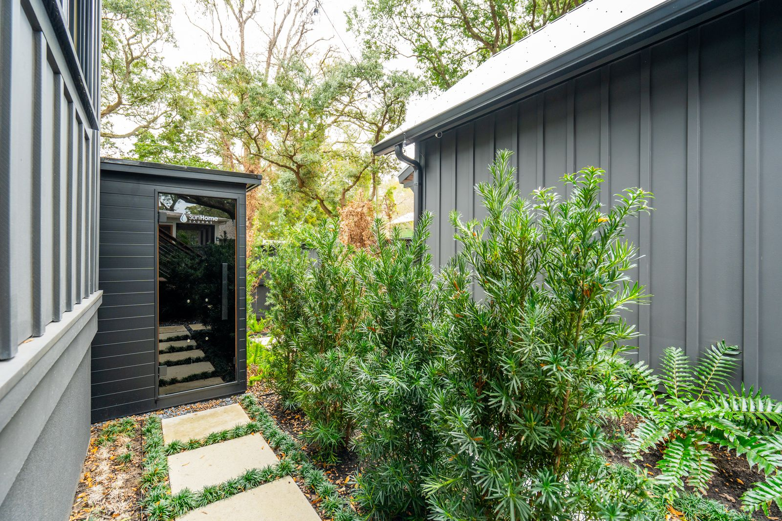 Further along a landscaped pathway, the sauna is tucked into its own secluded corner surrounded by dense greenery. 