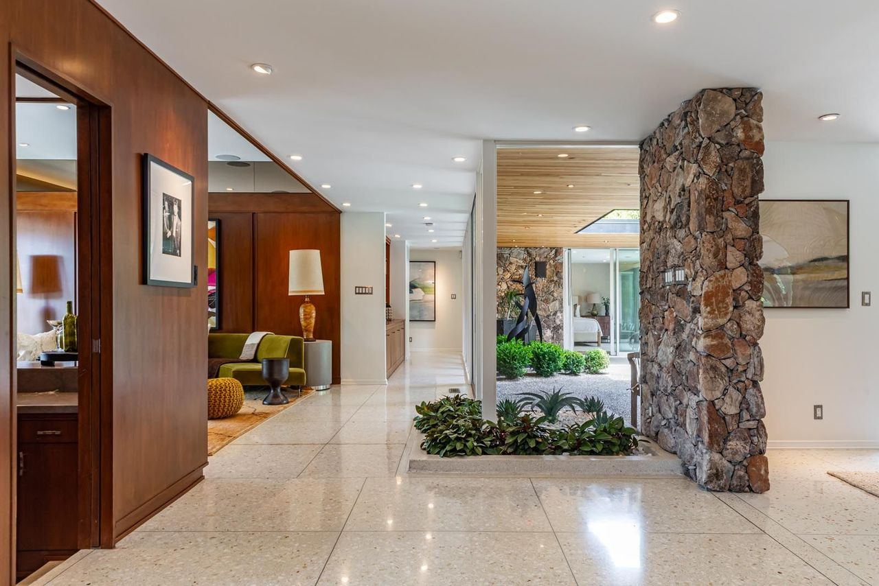 Stepping inside, the home opens into an expansive central gallery wrapped in terrazzo floors, bright white walls, and recessed lighting that stretches across the length of the residence. 