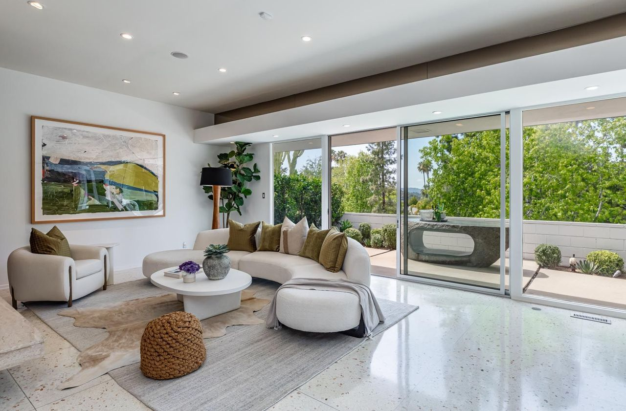 On the opposite wall, expansive sliding glass walls stretch across the room, opening the low-profile layout directly to an outdoor terrace.