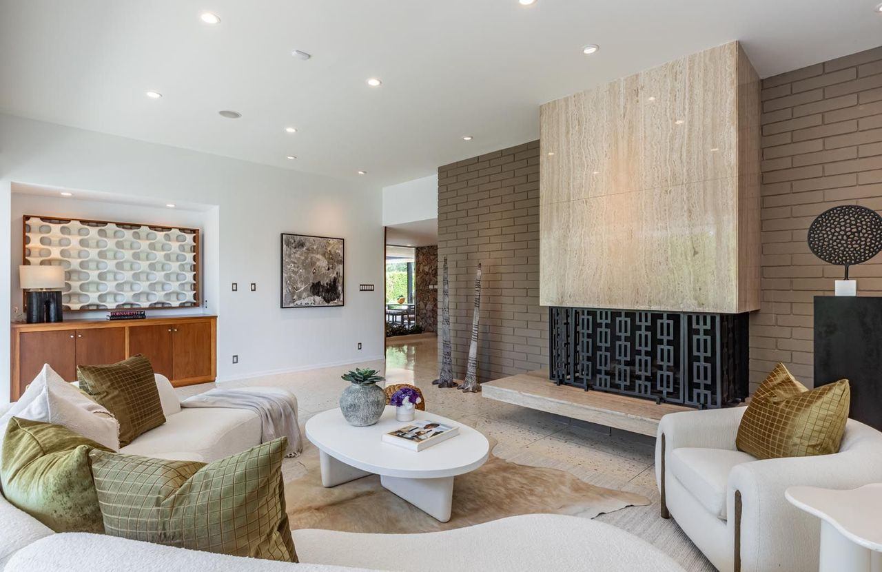 A floating stone fireplace sits on one side of the room, extending outward with a long built-in hearth that reinforces the room’s horizontal space.