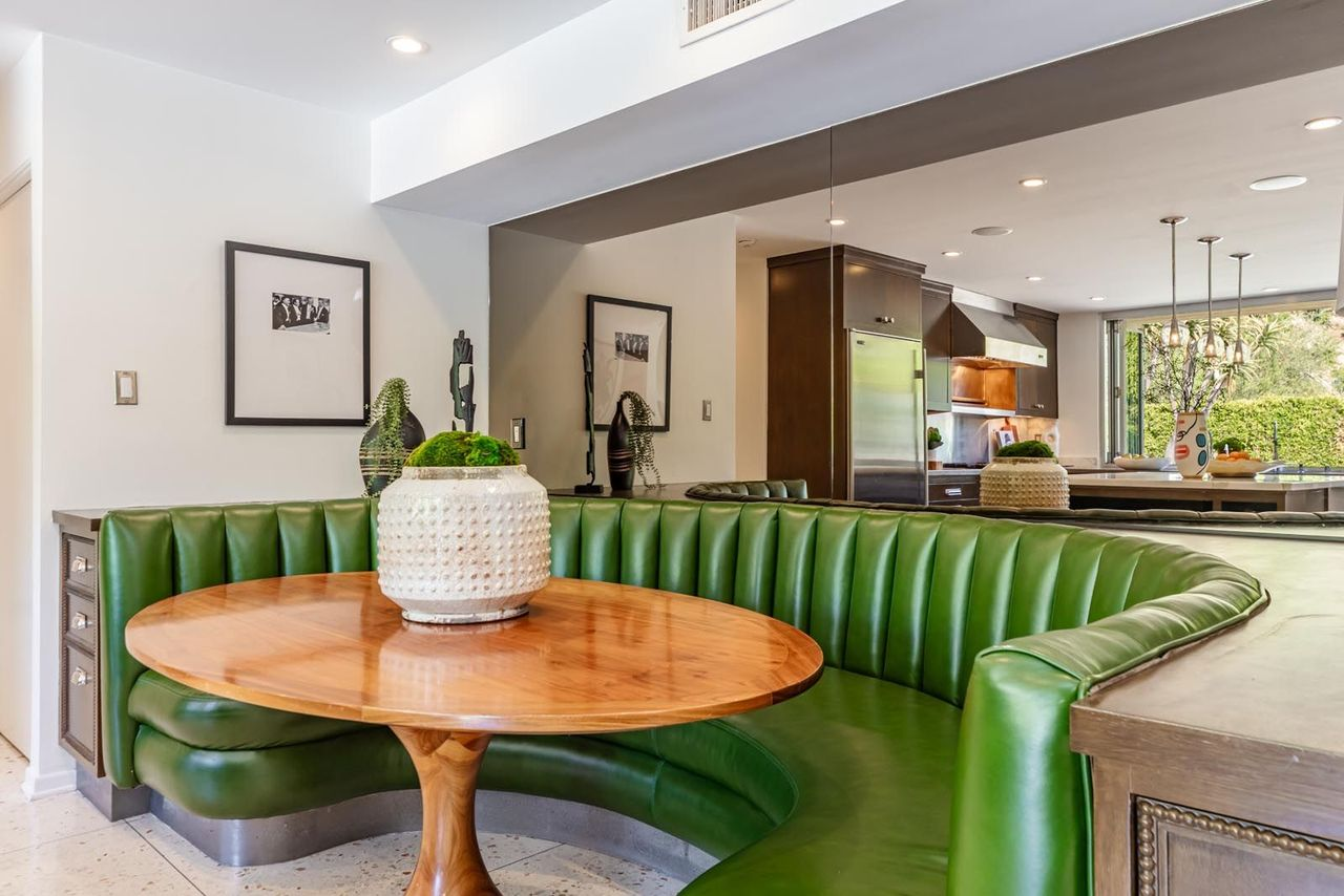 At one end of the kitchen, a built-in banquette dining nook softens the space with vibrant green seating curved around a wood table for casual dining.