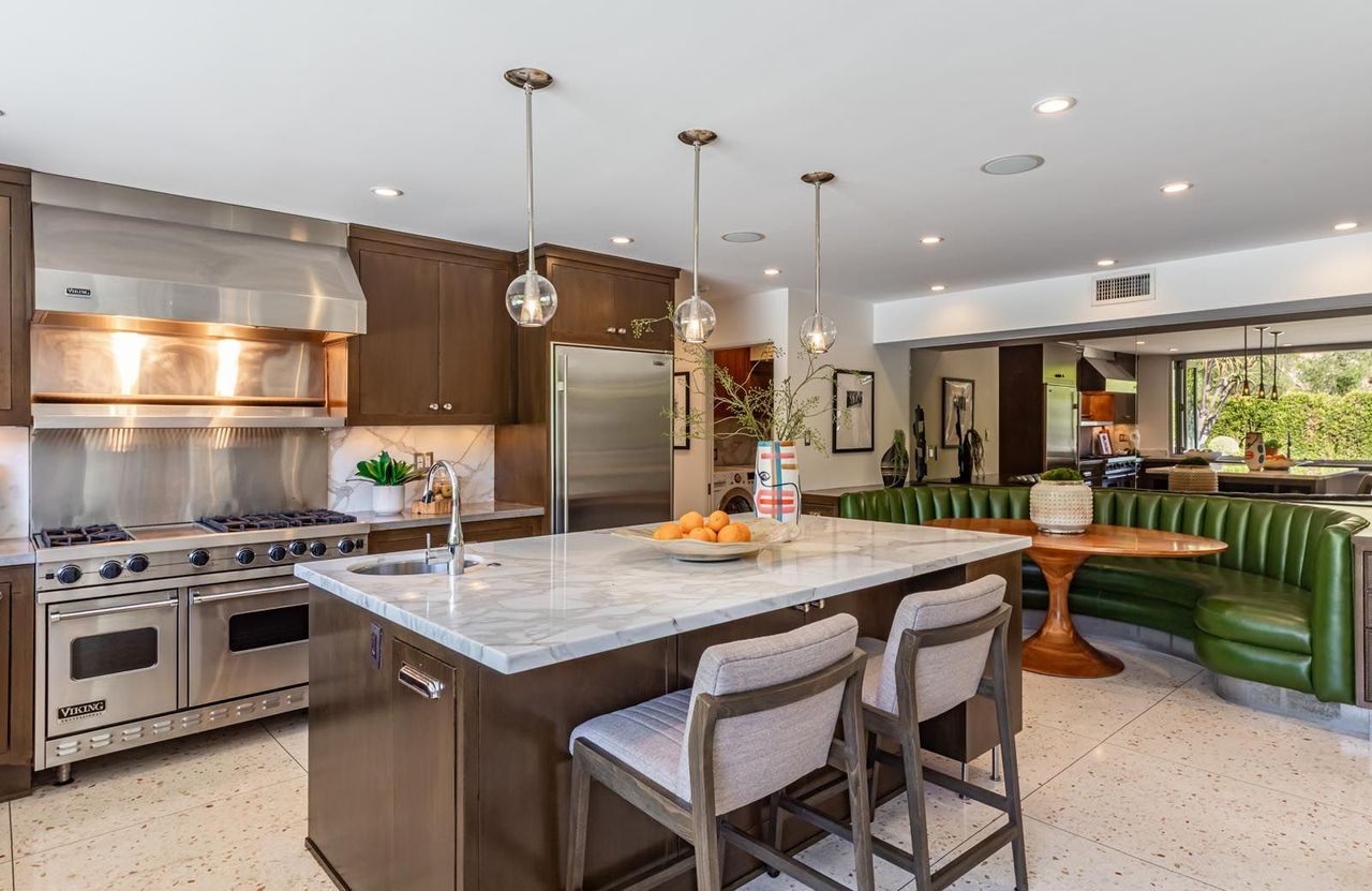 Connected to the dining room, the kitchen is centered around dark brown cabinetry and a large marble-topped island positioned beneath recessed lighting and simple pendant fixtures.