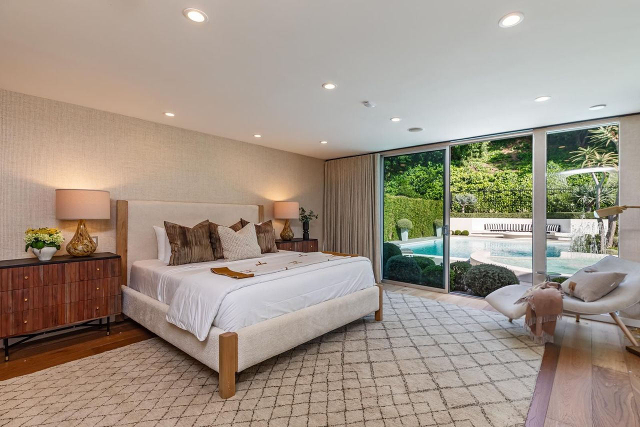 In the bedroom, a full wall of sliding glass doors stretches across the suite, framing the landscaped hillside while bringing in natural light.