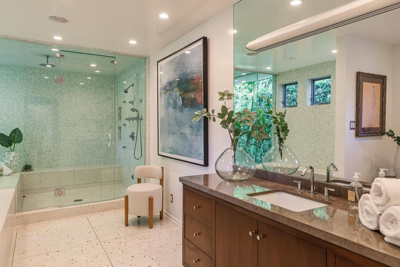 Inside the en-suite bathroom, terrazzo flooring continues from the rest of the home alongside dark cabinetry, long double vanities, and soft neutral finishes.