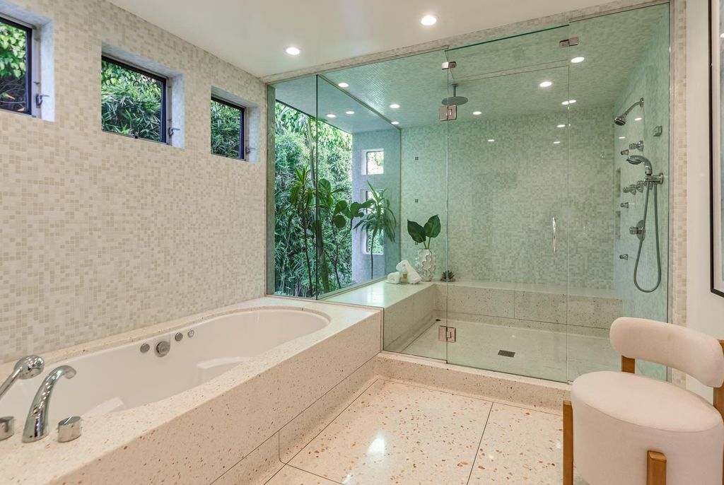 A large soaking tub and glass shower are positioned beside a floor-to-ceiling picture window overlooking dense bamboo landscaping, creating a private courtyard-like effect.
