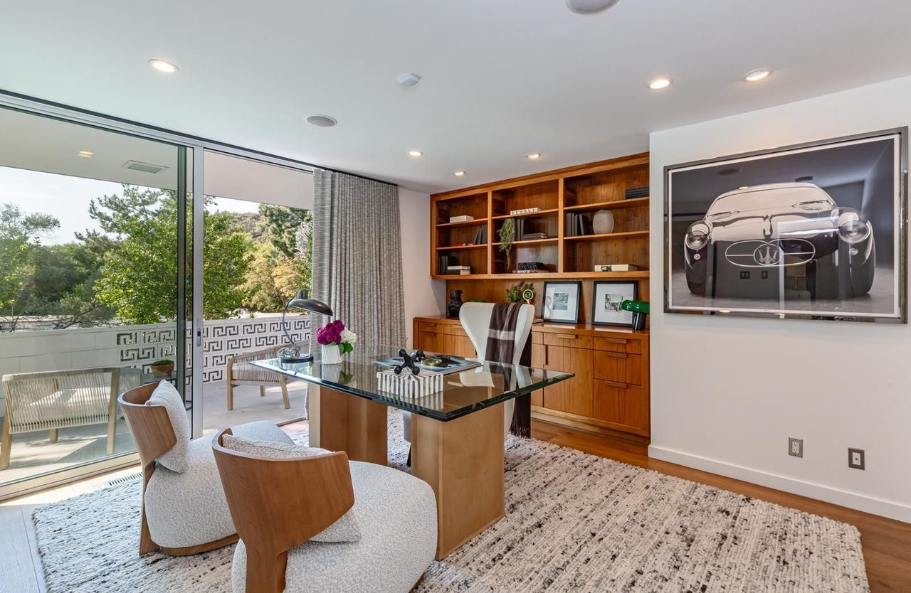 Built-in walnut shelving and cabinetry stretch across one wall, combining workspace storage with display areas for books, framed pieces, and collectibles.