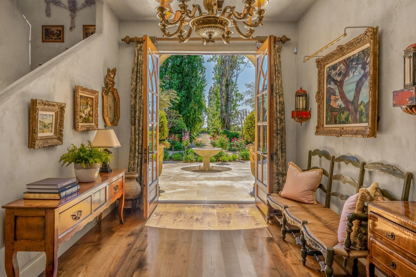 Stepping inside, the main house begins in a warm and intimate foyer with wide-plank wood floors, plaster-finished walls, antique-style furnishings, and a grand chandelier.