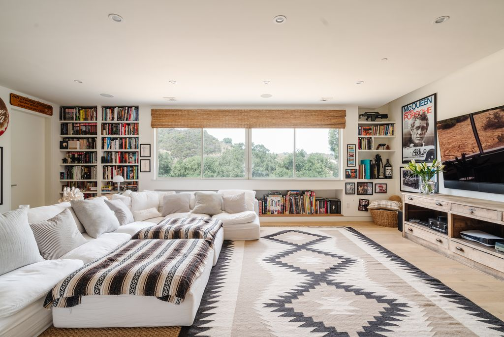 Down the hall, the home shifts into a more casual media room with a massive sectional that stretches across nearly the entire center of the room, facing a wall-mounted television.