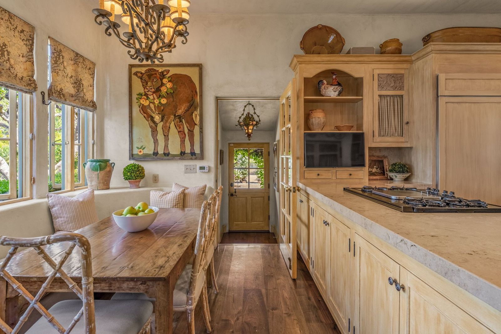Down the hall, the family kitchen seems to have a rustic French-country design with light wood cabinetry, plaster walls, and stone countertops.