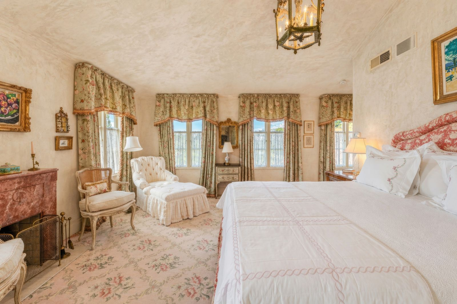 One of the bedroom suites in the main house pairs soft plaster walls and floral patterns with antique-inspired furnishings and layered textures.