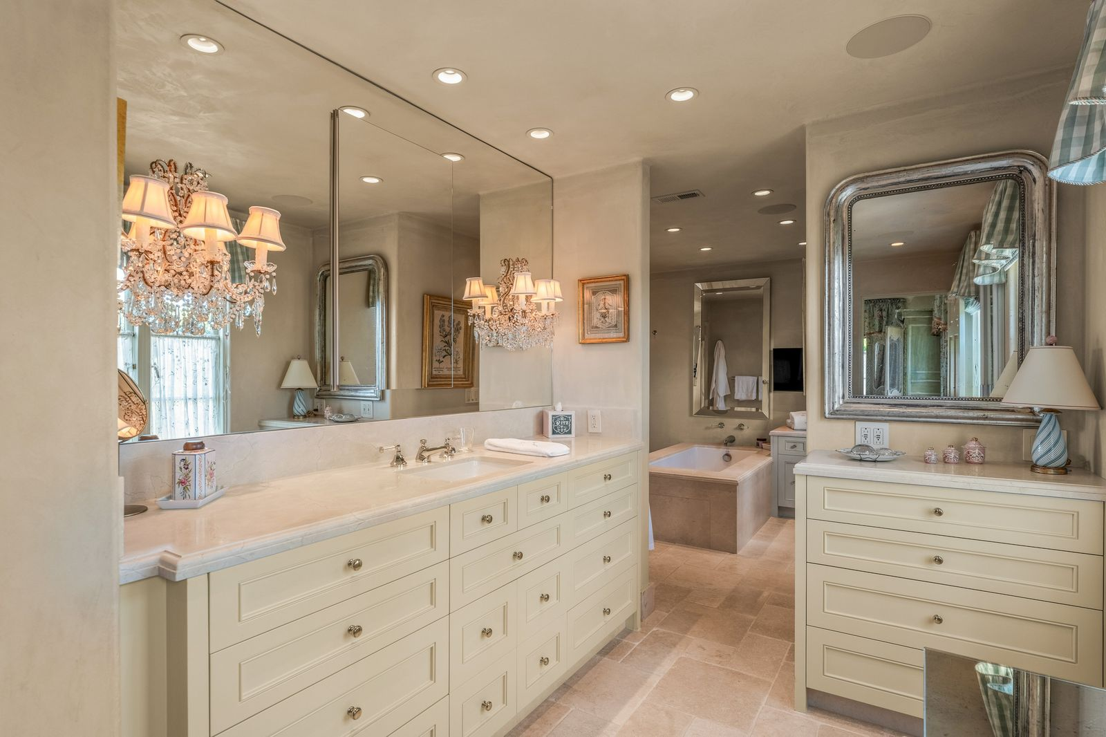The en-suite bathroom continues the traditional design with custom cream cabinetry, stone countertops, and crystal-style lighting fixtures that give the space a classic elegance.