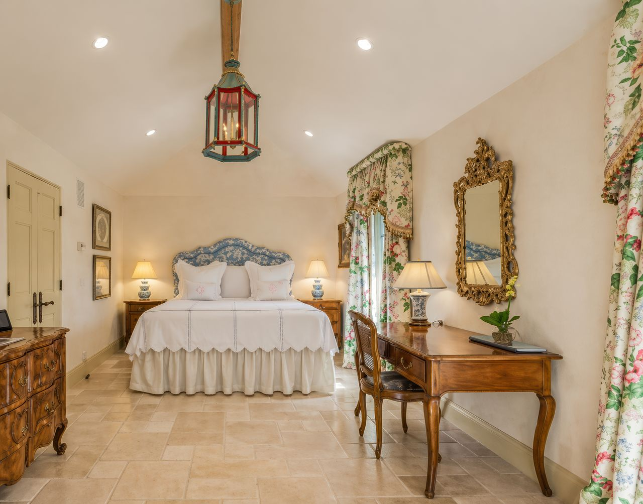 One of the guest bedrooms continues the estate’s romantic European design with soft plaster walls, limestone floors, and floral fabrics layered throughout the space.