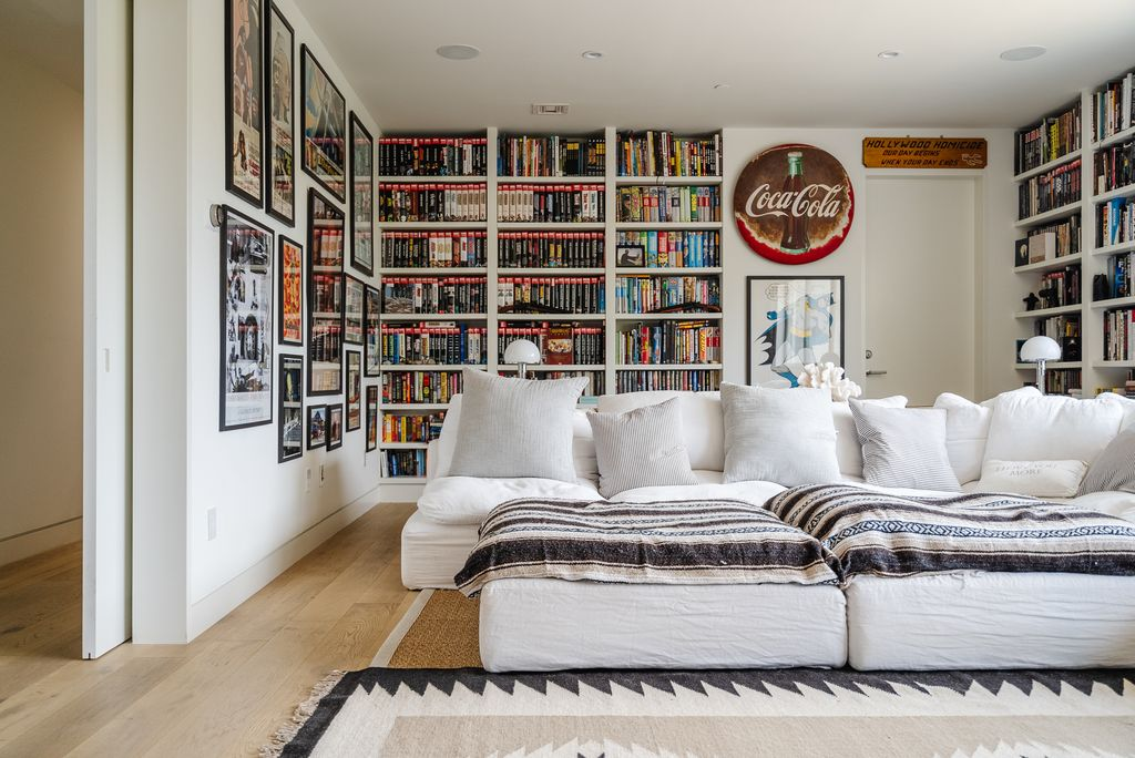 Built-in bookshelves wrap around multiple walls, packed with books, framed memorabilia, vintage signs, and movie posters that give the room a more personal and lived-in look.