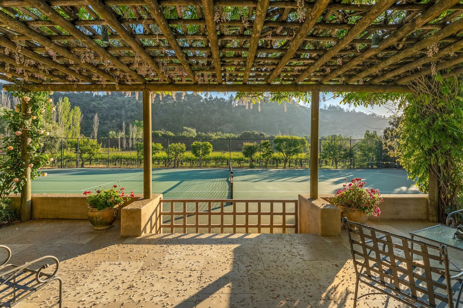 Set along the edge of the estate beside rows of vineyards, the tennis court is positioned next to a pergola-covered viewing terrace wrapped in climbing greenery.