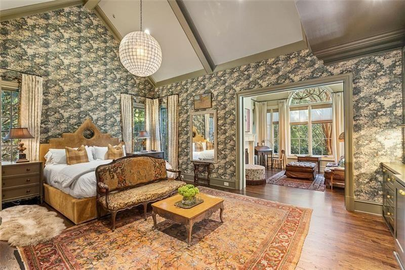 The bedroom opens up with patterned wallpaper, vaulted ceilings, and dark hardwood floors that contrast against the lighter upholstery. 