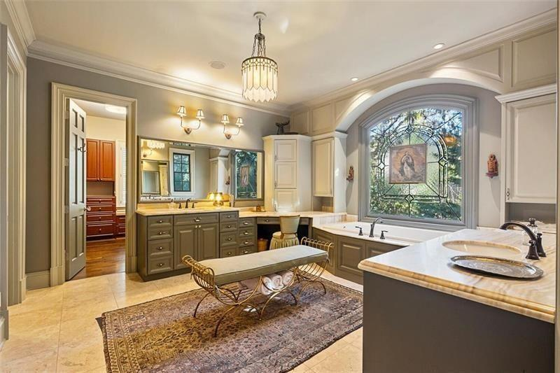 On the other side of the bedroom, the bathroom features dual vanities, custom cabinetry, and a soaking tub positioned beneath a decorative arched window.