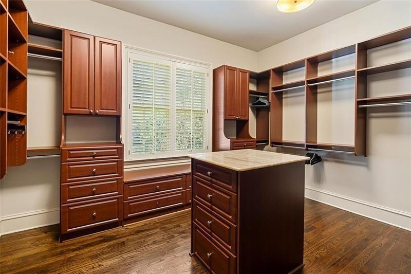Completing the suite, the walk-in closet is fully built out with custom wood cabinetry, open shelving, hanging storage, and a central island for additional organization.