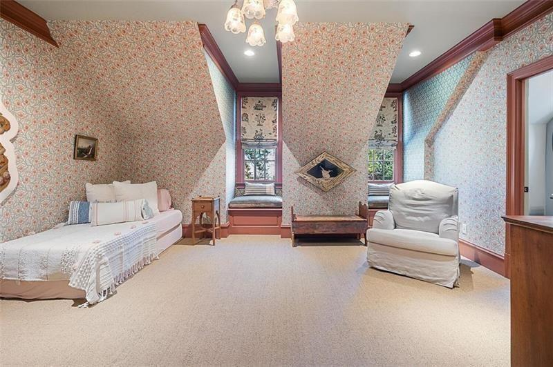 One bedroom leans softer and more traditional, with floral wallpaper wrapping both the angled ceilings and walls to create a cocoon-like effect beneath the roofline. 